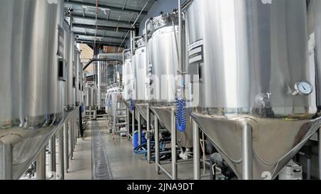 Rangée de cuves de micro-brasserie en métal brillant ou cuves de fermentation en purée dans l'usine de brasserie. Usine de bière moderne avec bouilloires, tubes et réservoirs à brasseur Banque D'Images