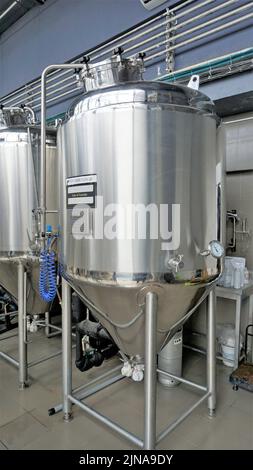 Rangée de cuves de micro-brasserie en métal brillant ou cuves de fermentation en purée dans l'usine de brasserie. Usine de bière moderne avec bouilloires, tubes et réservoirs à brasseur Banque D'Images