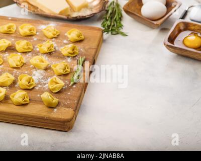 Cuisson de raviolis faits maison, boulettes farcies à la viande hachée - porc et boeuf. Boulettes sur une planche à découper en bois, ingrédients, branches de romarin Banque D'Images