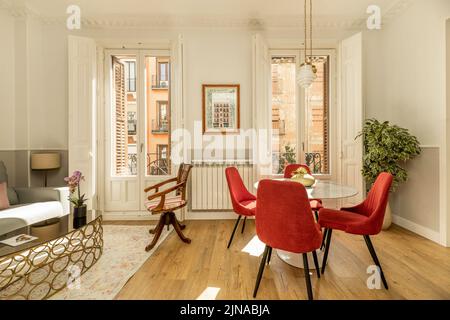 Salle de séjour dans l'appartement avec table latérale en métal et en verre, canapé deux places capitonné de tissu gris, table à manger ronde en marbre, chaises rembourrées Banque D'Images