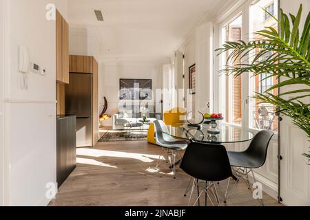 Salon de studio avec cuisine ouverte avec table ronde en verre, chaises en résine noire et balcons donnant sur la rue Banque D'Images