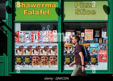 Un jeune homme qui marche à côté des affiches du Festival Fringe d'Édimbourg coincé sur la fenêtre d'une pizzeria à emporter. Banque D'Images