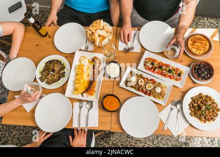 Table avec tapas, salades et cuisine espagnole typique autour de laquelle les gens sont prêts à manger. Concentrez-vous sur les plaques centrales. Banque D'Images