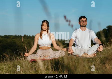 Jeune couple adulte méditant à l'extérieur, femme caucasienne et homme vêtu respirent de l'air frais dans la nature Banque D'Images