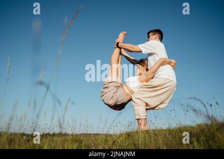 Homme et femme vêtus faisant la pose difficile tout en pratiquant le yoga en plein air sur le terrain avec Blue Sky sur le fond Banque D'Images