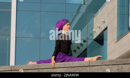 Jeune femme musulmane calme dans hijab arabe islamique femme indienne fille yogi assis sur la ficelle à l'extérieur dans la rue enjoing bon stretching sport yoga Banque D'Images