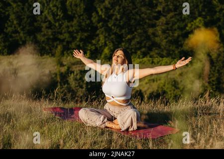 Une jeune femme se bronzer et méditer sur le Mat à l'extérieur au coucher du soleil avec un paysage magnifique sur l'arrière-plan Banque D'Images