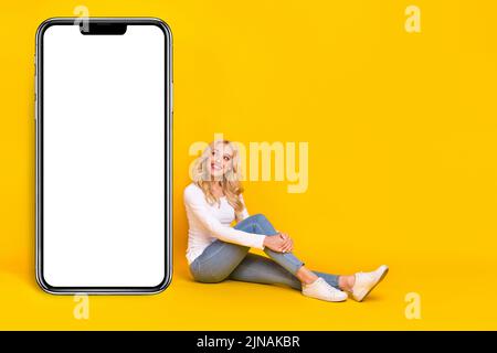 Photo pleine grandeur de belle femme blonde millénaire assis look promo habillement chemise jeans chaussures isolées sur fond jaune Banque D'Images