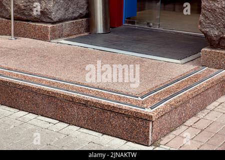 entrée avec seuil en granit avec caoutchouc antidérapant pour faire du shopping depuis le trottoir piétonnier, de la plieuse sur le tapis de sol à la porte en verre, façade en pierre rugueuse de Banque D'Images