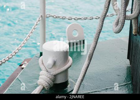 Une corde épaisse blanche se trouve sur le bollard d'amarrage du navire sur la jetée. Le bateau dévie sur l'eau qui s'indéchirable. Corde d'amarrage tenue par un nœud de récif contre la fermeture de la chaîne métallique Banque D'Images