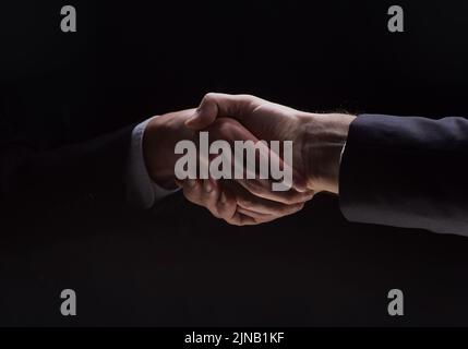 Photo de deux hommes en costume se serrant les mains sur un fond noir Banque D'Images