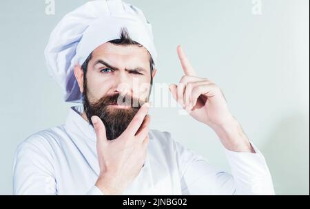 Chef professionnel pointant du doigt vers le haut. Homme à barbe pensive en uniforme de cuisson. Cuisine nouvelle idée. Banque D'Images