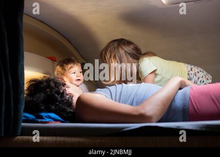 Un jeune père caucasien et deux enfants s'amusent sur un lit en cabine dans un camping-car ou un camping-car. Vacances en camping-car avec enfants. Banque D'Images