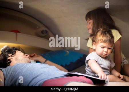 Un jeune père caucasien et deux enfants s'amusent sur un lit en cabine dans un camping-car ou un camping-car. Vacances en camping-car avec enfants. Banque D'Images