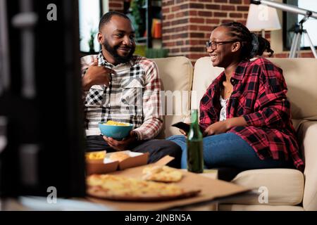 Petite amie et petit ami manger des plats à emporter et changer de chaîne à la télévision, à la recherche de film. Profitez d'un repas de livraison à emporter et d'une bière devant un film télévisé ou une activité de loisirs. Banque D'Images