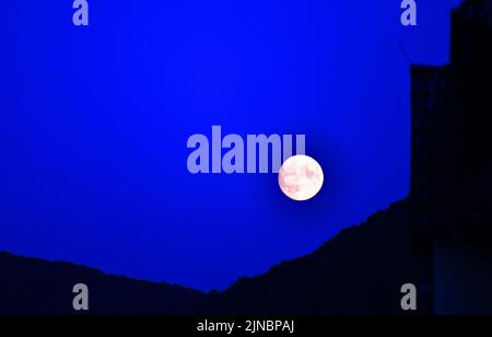 La lune s'élève derrière une montagne Banque D'Images