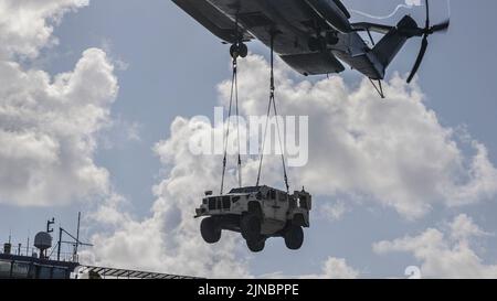 Les Marines des États-Unis avec le Medium Tiltrotor Squadron 262 (rein.), 31st Marine Expeditionary Unit transportent un véhicule tactique léger conjoint avec un Super Stallion CH-53E au-dessus de la base mobile expéditionnaire USS Miguel Keith (ESB-5) lors d'un exercice d'équipe de soutien d'hélicoptère en mer des Philippines, le 8 août 2022. Les HSTs permettent de configurer une zone de dépôt rapide pour le ramassage et le transport d'équipements lourds en vol. Le MEU de 31st opère à bord de navires du Groupe amphibie Ready de Tripoli dans la zone d'opérations de la flotte de 7th pour améliorer l'interopérabilité avec les alliés et les partenaires et servir de réponse prête à l'emploi Banque D'Images