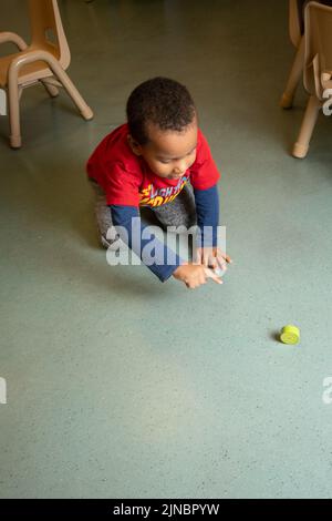 Éducation préscolaire garde d'enfants 2-3 ans garçon roulant autour bloc excité de regarder le roulement, le pointant vers elle Banque D'Images