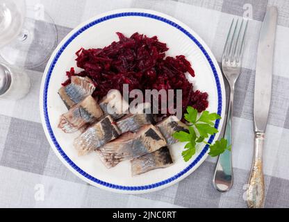 Salade de hareng appétissante avec betteraves, crème sure et persil dans une assiette blanche Banque D'Images