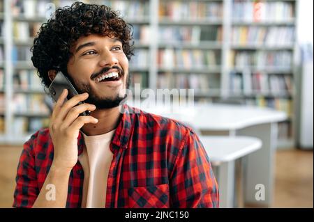 Conversation téléphonique. Gros plan d'un homme heureux aux cheveux bouclés et aux cheveux d'un indien ou d'un arabe, qui a négocié avec un smartphone, s'entretient avec un ami ou un collègue, regarde loin, souriant et amical Banque D'Images