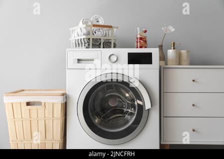 Lave-linge avec panier, serviettes et capsules près du mur lumineux dans la buanderie Banque D'Images