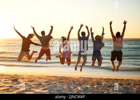 Sautez et laissez la mer vous libérer. Vue arrière d'un groupe de jeunes amis qui sautent dans les airs à la plage. Banque D'Images