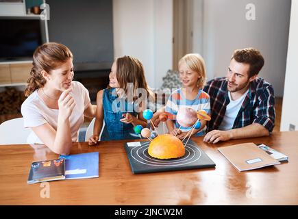 Faire de l'éducation une chose familiale. Une belle jeune famille travaillant ensemble sur un projet scientifique à la maison. Banque D'Images