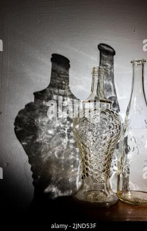 Deux bouteilles millésimes transparentes et une ombre abstraite de celles-ci sur le mur. Banque D'Images