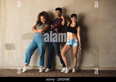 Étaient une équipe moyenne. Portrait d'un groupe de jeunes amis joyeux posant pour une photo tout en se penchant contre un mur à l'extérieur pendant la journée. Banque D'Images