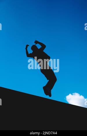 Silhouette noire dans l'air d'un homme faisant un somersault extrême avec le ciel en arrière-plan. Homme entraînement gymnastique à l'extérieur. Banque D'Images