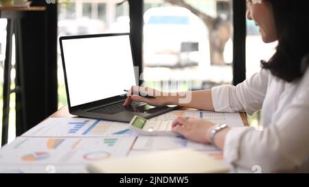 Vue de côté investisseur féminin professionnel analysant des graphiques financiers graphiques dans un bureau moderne lumineux Banque D'Images