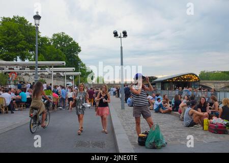 Les gens, surtout les touristes, traînent en petits groupes avec de la nourriture et des boissons le long de la Seine. Belle journée d'été en plein air à Paris, France. Banque D'Images