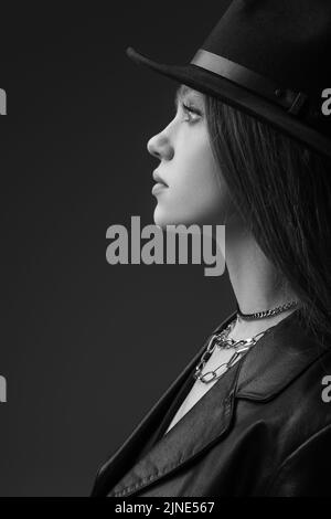 profil de l'adolescent modèle dans chapeau fedora posant en studio, photo monochrome Banque D'Images