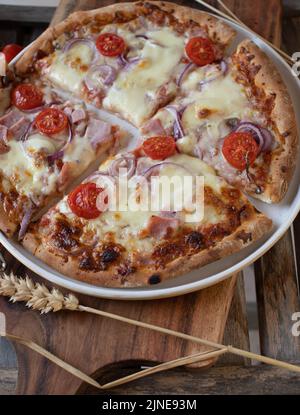 Pizza au jambon et au fromage, tomates cerises et oignons rouges sur fond de bois Banque D'Images