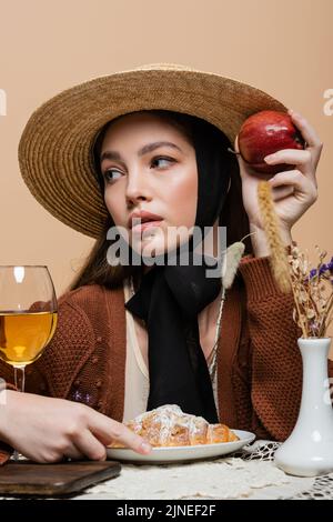 Modèle élégant, avec pomme près d'un croissant et vin sur table, isolé du beige Banque D'Images