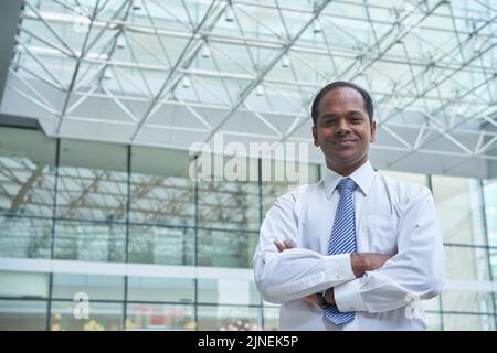 Homme d'affaires indien souriant debout avec ses bras croisés et regardant la caméra Banque D'Images