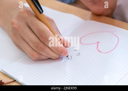 Main d'un enfant dessinant des coeurs dans un carnet. Une déclaration secrète d'amour. L'enfant rêve de l'amour. Banque D'Images