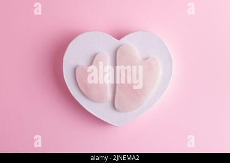 Pierres sha de gua de quartz rose pour la relaxation du visage et du corps et le massage de levage. Composition minimaliste avec masseurs à pression sur un hea en papier décoratif Banque D'Images