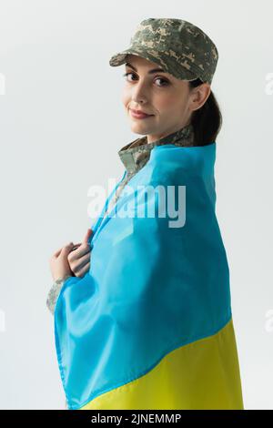 Jeune femme en uniforme militaire couvrant avec drapeau ukrainien isolé sur image grise, stock Banque D'Images