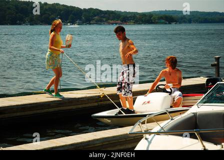 Une femme adulte aide deux adolescents à amener leur petit bateau sur le quai pour se mettre à l'eau lors d'une belle journée de vacances d'été sur le lac Banque D'Images