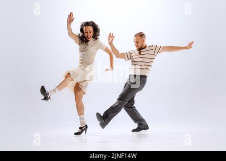 Rythme et expression. Couple de danse énergique dans des tenues de style rétro dansant lindy hop, jive isolé sur fond blanc. 50s, 60s, 70s américain Banque D'Images