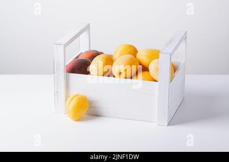 Boîte en bois avec abricots et pêches isolés sur fond blanc Banque D'Images