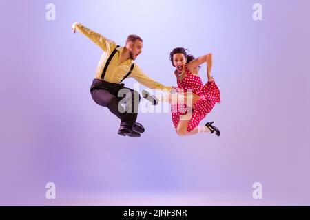 Couple de danseurs émotif lumineux dans le style rétro coloré attires dansant des danses incendiaires isolées sur fond violet dans la lumière de néon. Banque D'Images