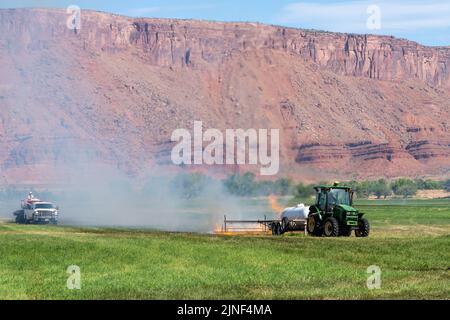 Un tracteur tire un brûleur au propane pour brûler les mauvaises herbes dans un champ de foin après avoir coupé la luzerne dans un ranch de l'Utah. Un camion-citerne suit pour contrôler le sapin Banque D'Images