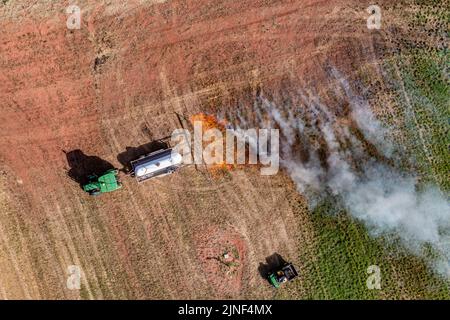 Un tracteur tirant un brûleur de propane brûle les mauvaises herbes dans un champ de foin après avoir coupé la luzerne dans un ranch de l'Utah. Banque D'Images