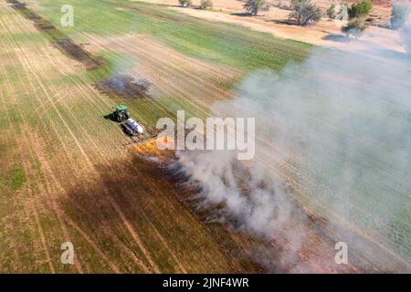 Un tracteur tirant un brûleur de propane brûle les mauvaises herbes dans un champ de foin après avoir coupé la luzerne dans un ranch de l'Utah. Banque D'Images