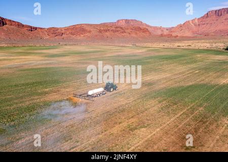 Un tracteur tirant un brûleur de propane brûle les mauvaises herbes dans un champ de foin après avoir coupé la luzerne dans un ranch de l'Utah. Banque D'Images