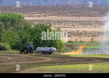 Un tracteur tirant un brûleur de propane brûle les mauvaises herbes dans un champ de foin après avoir coupé la luzerne dans un ranch de l'Utah. Banque D'Images