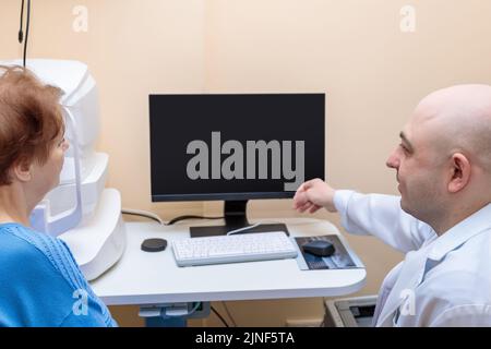 Un ophtalmologiste masculin explique les résultats d'un examen oculaire à une femme adulte, montrant un dessin sur un ordinateur. Banque D'Images