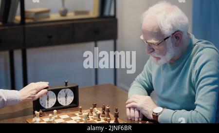 gris cheveux homme pensant près de chessboard et ami fixant le temps sur l'horloge d'échecs, image de stock Banque D'Images